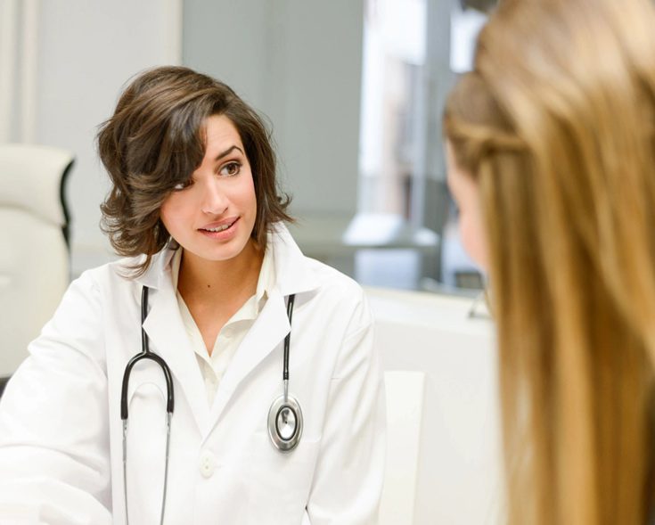 A woman in white coat sitting on chair near a wall.